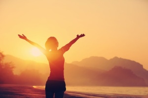 Joyful woman with raised arms at sunrise